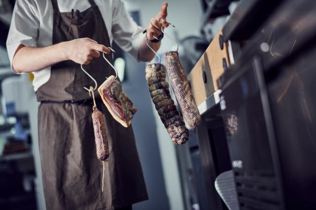 a chef carries various meats on hooks near a Foster counter